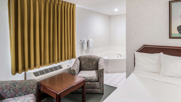 Une chambre d’hôtel comprenant un lit, une chaise, une table, une salle de bain avec baignoire et une fenêtre avec des rideaux.