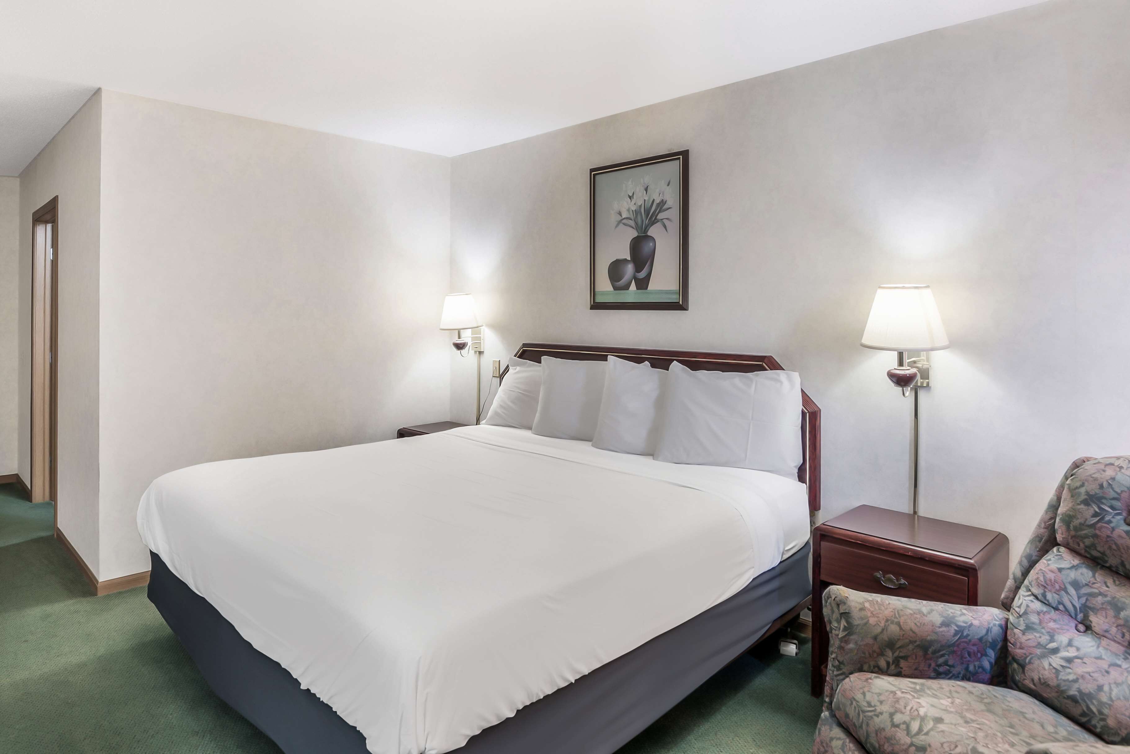 Una camera d'albergo con un letto grande, due comodini con lampade, una poltrona in stile floreale e un'opera d'arte appesa alla parete.
