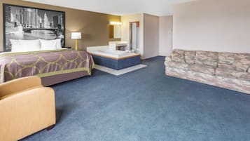 Habitación de hotel con una cama grande, un área de descanso con sofá, una mesita, un escritorio y un baño con bañera y lavamanos.