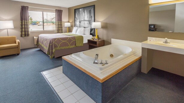 A hotel room with a bed, a large bathtub, a sofa, a desk, and a bathroom with a sink and mirror. - Super 8 by Wyndham Hebron Lowell Area (Hebron)