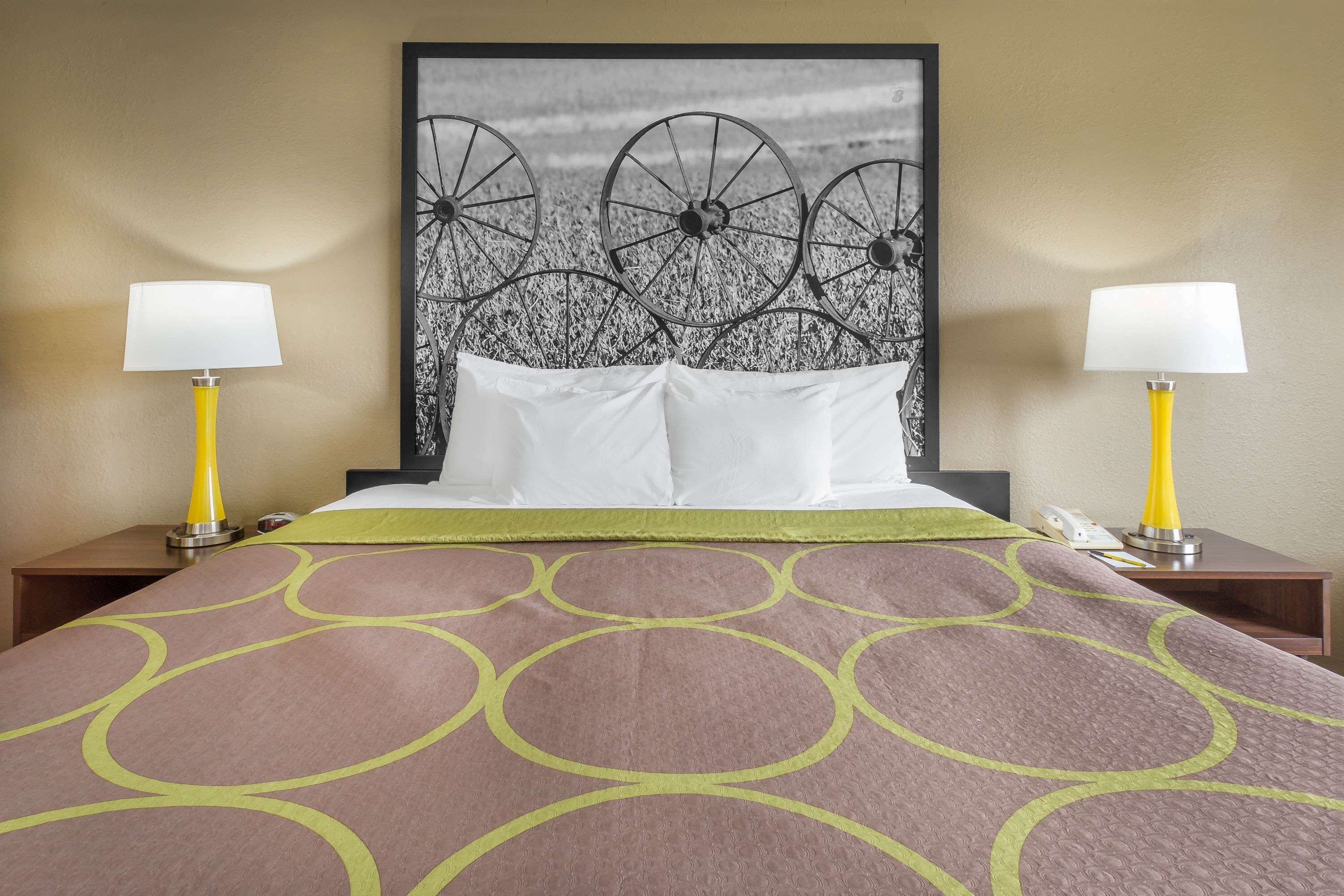 A hotel room with a large bed, two bedside lamps, a headboard with a wheel design, and a patterned bedspread.