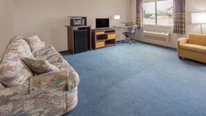A hotel room with a large floral-patterned sofa, a small TV, a desk with a computer, a chair, and a window with curtains. - Super 8 by Wyndham Hebron Lowell Area (Hebron)