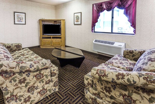 A living room with floral-patterned sofas, a flat-screen TV, a wooden cabinet, and a window with purple curtains.