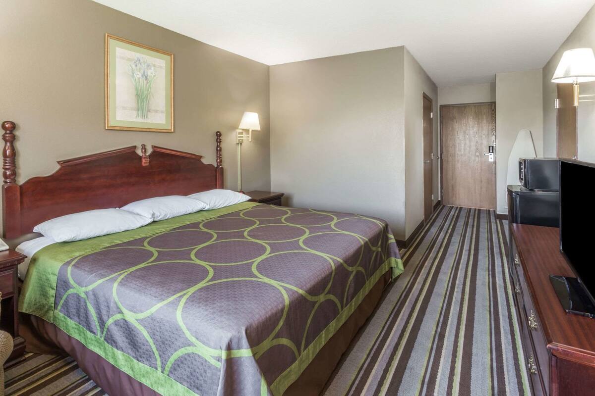 Une chambre d’hôtel comprenant un lit, des lampes de chevet, une télévision et une porte donnant sur une autre pièce.
