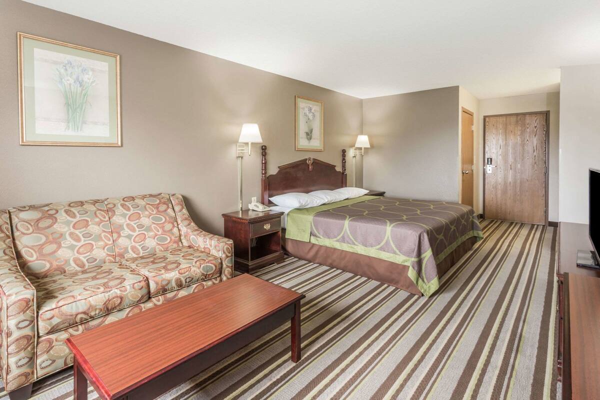 Une chambre d’hôtel avec un lit, un canapé, une table de chevet, une lampe, une télévision et une porte.