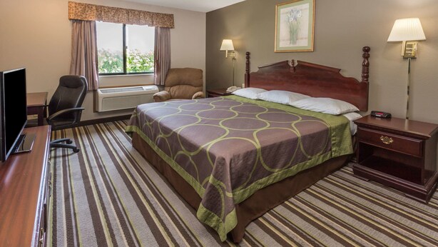 Une chambre d’hôtel avec un grand lit, un bureau avec un ordinateur, une chaise, une fenêtre avec des rideaux et deux lampes de chevet.