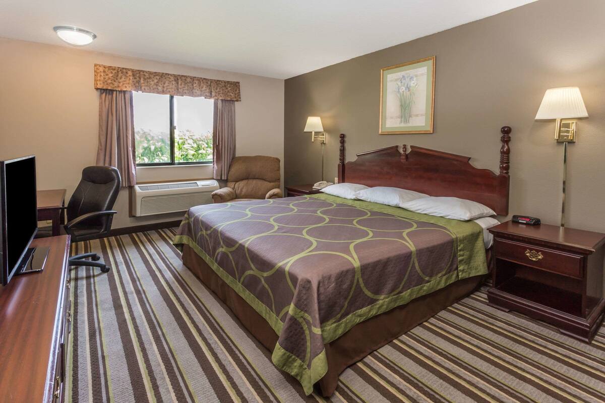 Une chambre d’hôtel avec un grand lit, un bureau avec un ordinateur, une chaise, une fenêtre avec des rideaux et deux lampes de chevet.