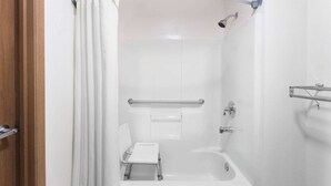Une petite douche à l’italienne blanche, dotée d’un pommeau de douche, d’un pommeau de douche à main, d’une barre d’appui et d’un petit marchepied.