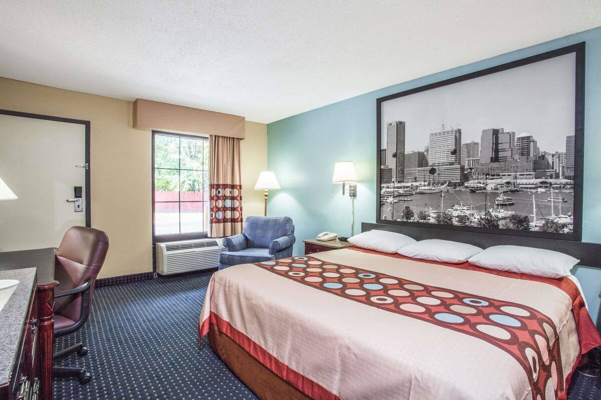 Habitación de hotel con cama, escritorio, silla y una pintura de un paisaje urbano en la pared.