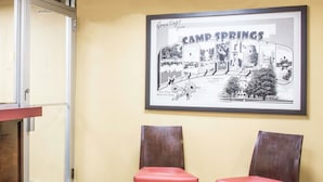 Un cuadro enmarco de Camp Springs colgado en una pared, dos sillas de madera con cojines rojos y una puerta con un panel de vidrio.