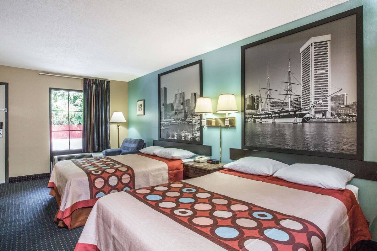 Habitación de hotel con dos camas, un cuadro de un paisaje urbano y una ventana con cortinas.