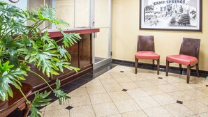 Zona de recepción con una planta, dos sillas rojas, un cuadro en la pared y un reloj.