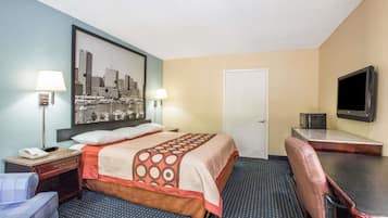 Habitación de hotel con cama, escritorio con silla, televisor y un cuadro de paisaje urbano en la pared.
