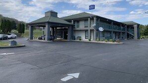 Een hotel met twee verdiepingen, een overdekte ingang, schotels en een parkeerplaats.