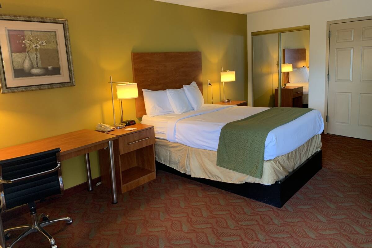 Una habitación de hotel con cama, mesitas de noche, escritorio, silla y espejo.