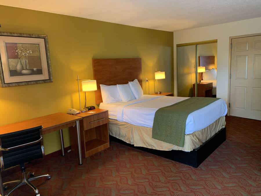 A hotel room with a bed, bedside tables, a desk, a chair, and a mirror.