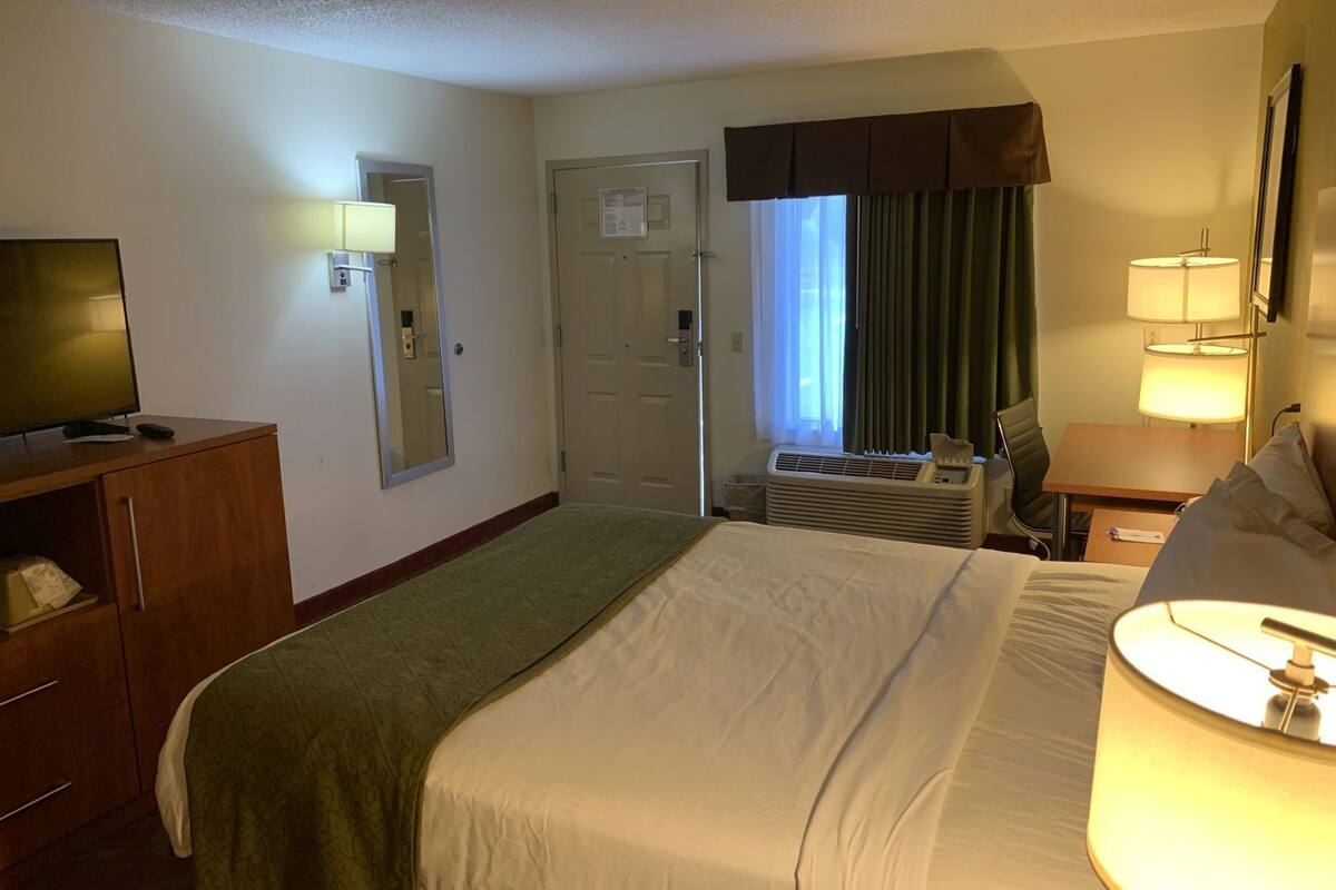 Una habitación de hotel con cama, televisión, escritorio, lámpara y ventana con cortinas.