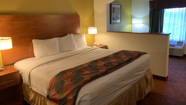 Een hotelkamer met een groot bed, twee bedlampen, een houten hoofdeinde, een spiegel en een raam met gordijnen.