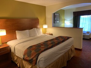 Ein Hotelzimmer mit einem großen Bett, zwei Nachttischlampen, einem Holzkopfstück, einem Spiegel und einem Fenster mit Vorhängen.