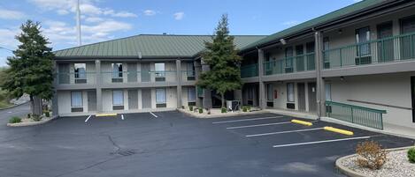 Un Baymont Inn & Suites con un edificio de dos plantas, estacionamiento y árboles verdes.