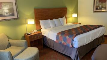 A hotel room with a large bed, a nightstand with a lamp, a chair, and a framed picture on the wall.