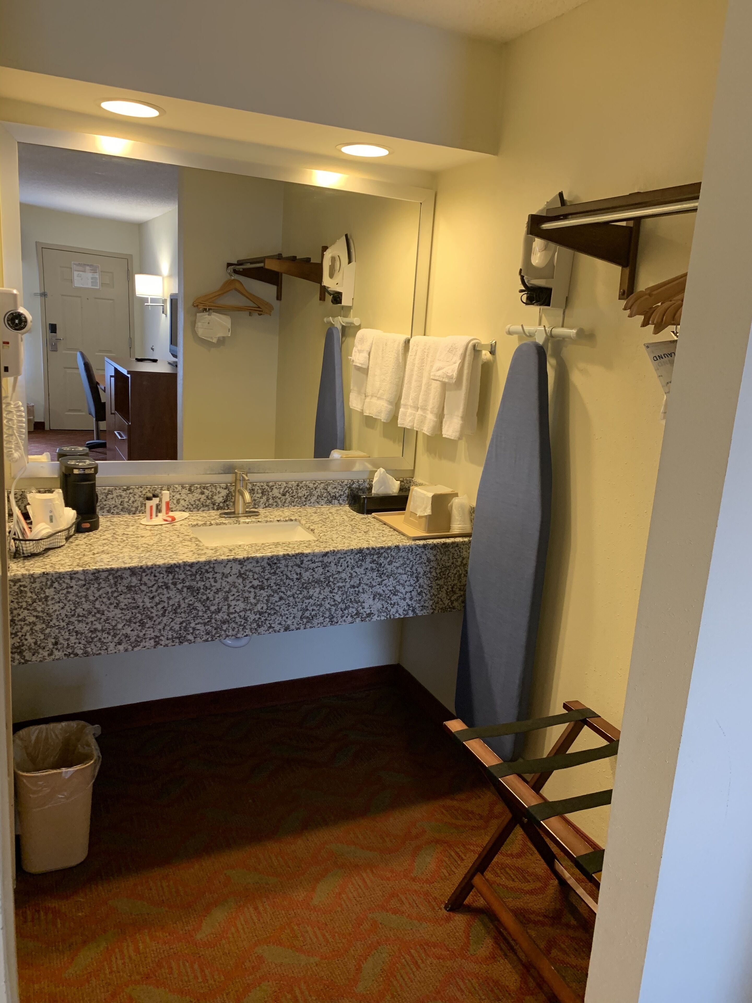 A hotel bathroom with a granite countertop, a sink, a mirror, a towel rack, and a hanging shower curtain.