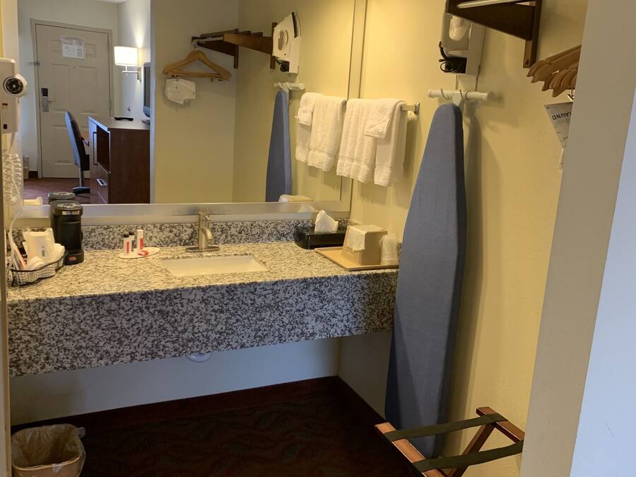 A hotel bathroom with a granite countertop, a sink, a mirror, a towel rack, and a hanging shower curtain.