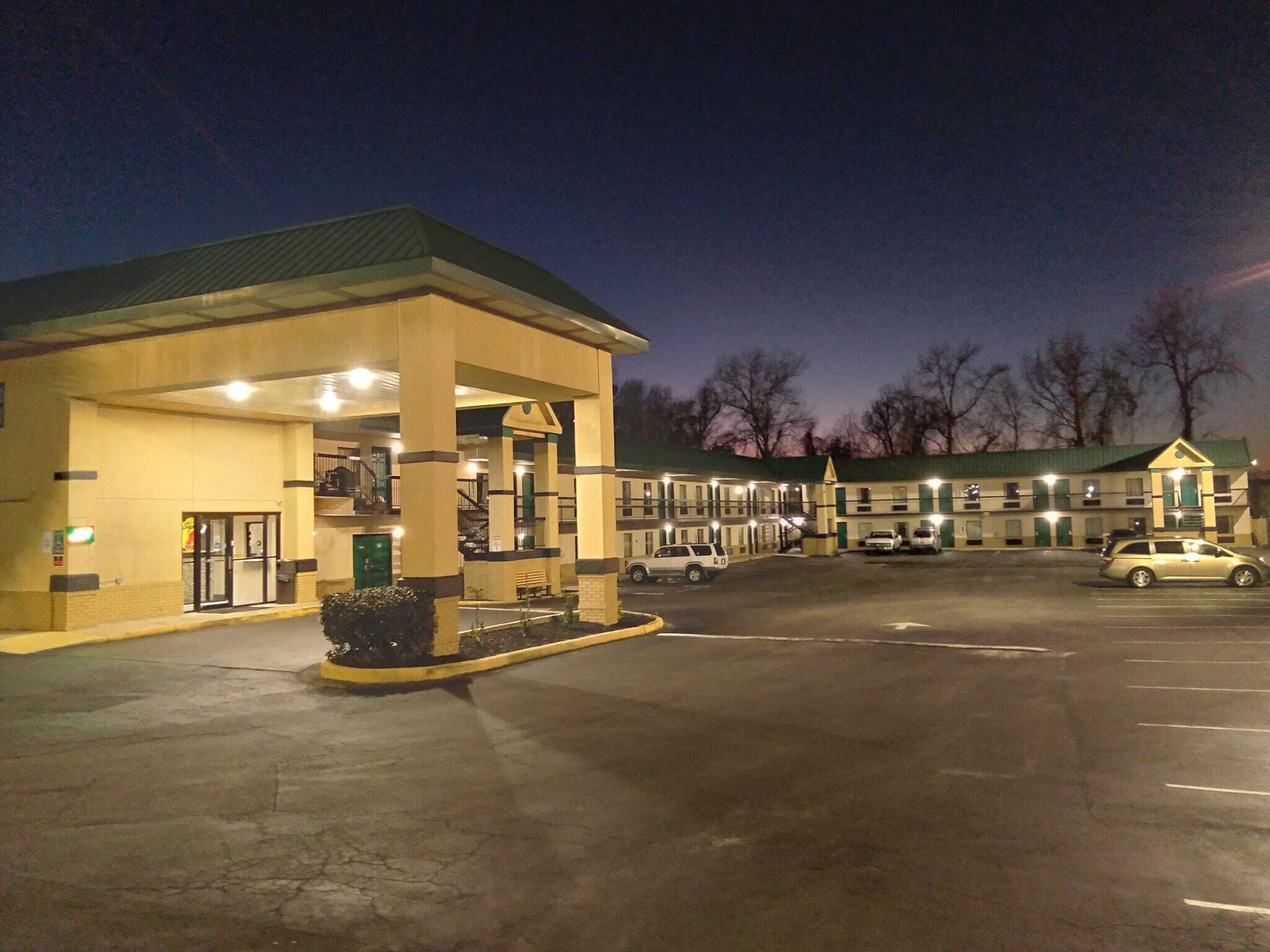 A motel with a gas station attached, featuring a large parking lot and a building with multiple windows.