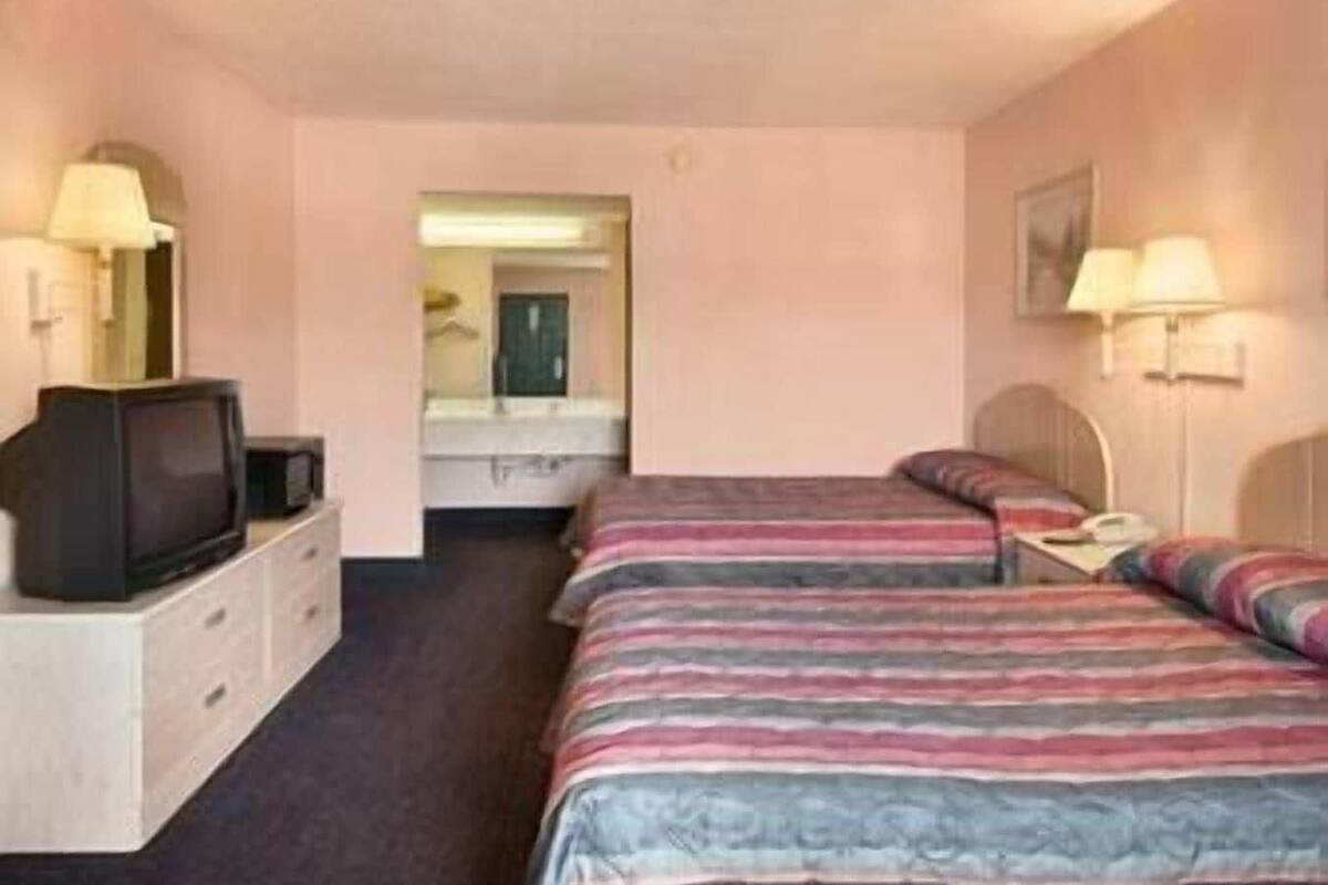 A hotel room with two beds, a television, a dresser, and a mirror.