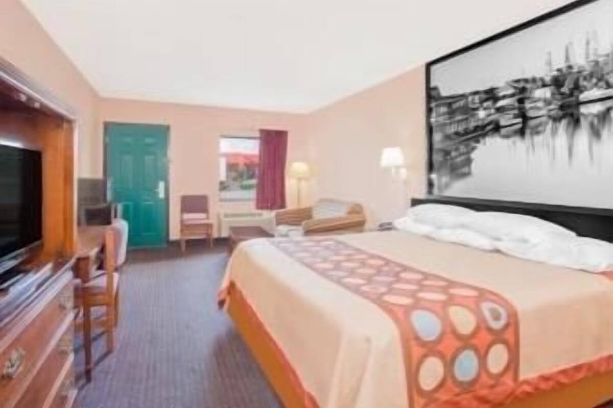 A hotel room with a bed, a desk, a chair, a television, and a painting on the wall.