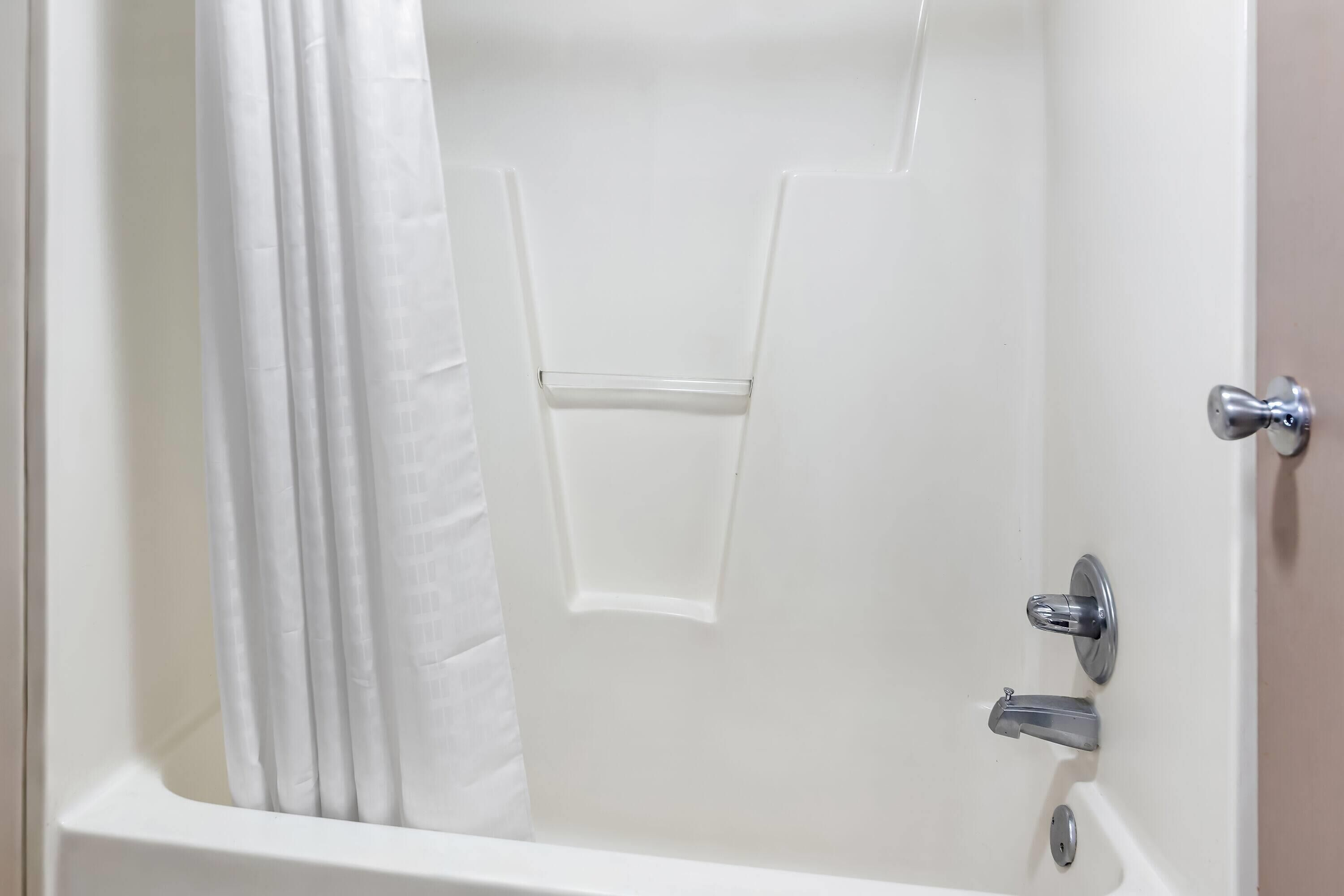 Una bañera blanca con cortina de ducha, un grifo y un tirador.