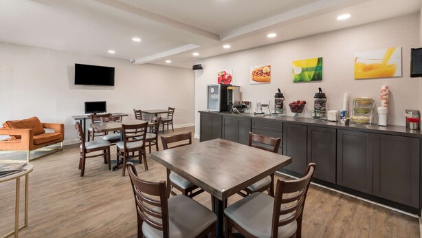 A modern kitchen and dining area with a flat-screen TV mounted on the wall, wooden dining table and chairs, and a kitchen counter with various appliances and decor. - Quality Inn Gastonia East (Gastonia)