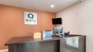 A reception desk with a sign reading "Quality by Choice Hotels," a computer, a phone, and a bottle of hand sanitizer. - Quality Inn Gastonia East (Gastonia)