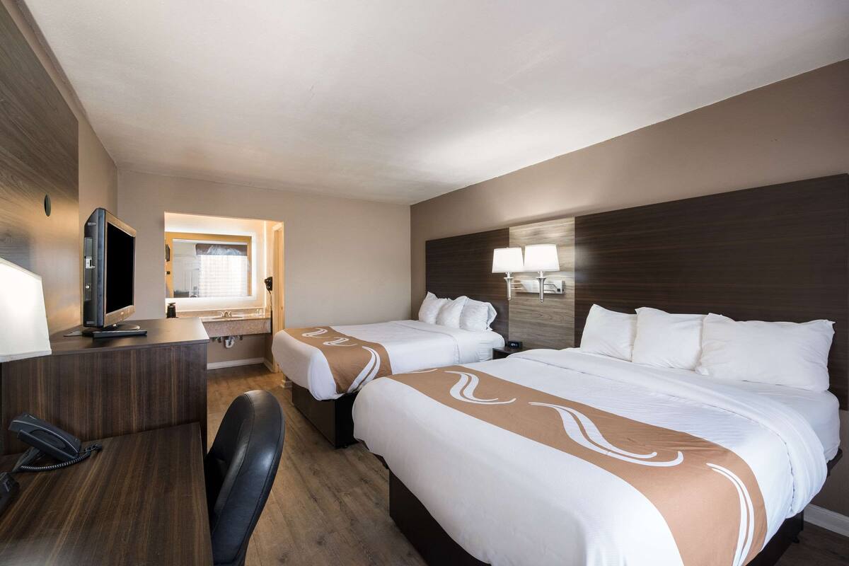 A hotel room with two beds, a desk with a computer, a chair, and a TV.