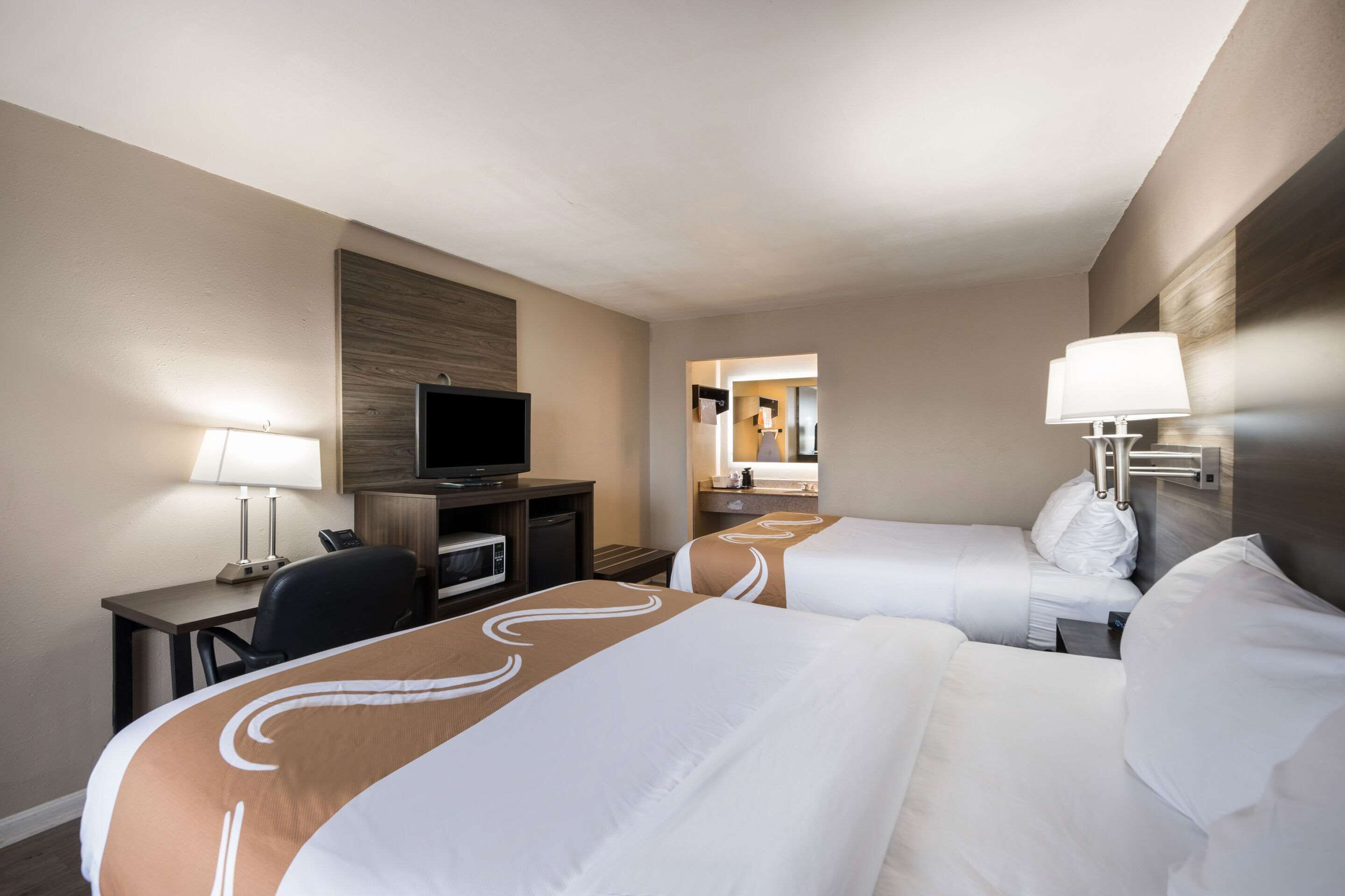 A hotel room with two beds, a desk with a lamp, a television, and a mirror.