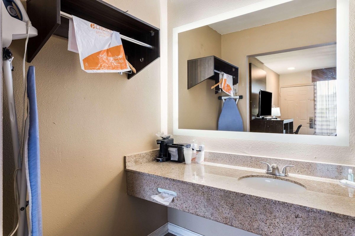 Un baño de hotel con encimera de granito, lavamanos, espejo, toallero y televisor.