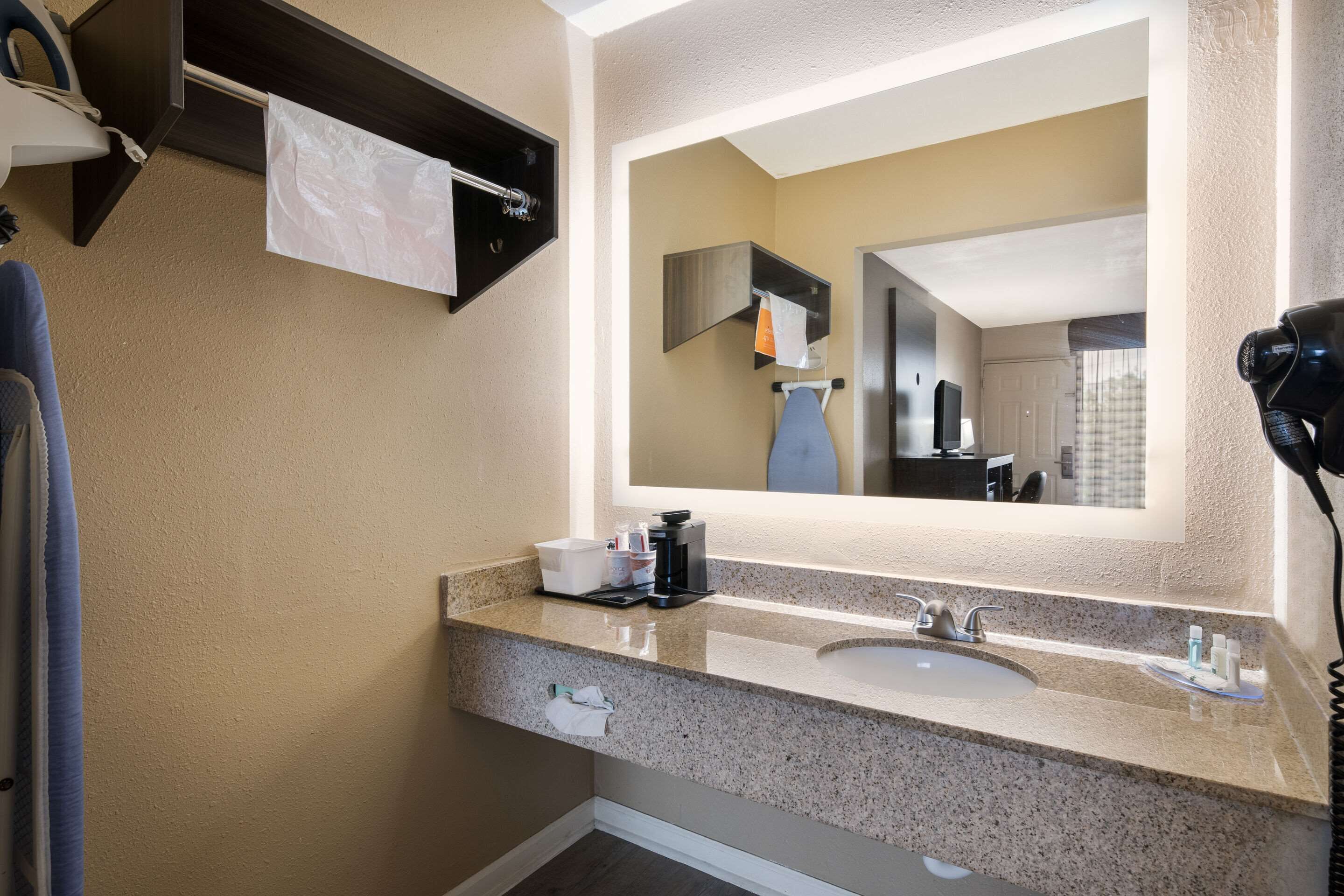 Un baño con encimera de granito, un lavabo, un espejo, un perchero y un secador de pelo.
