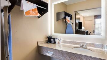 Une salle de bain d’hôtel avec un lavabo doté d’un plan de travail en granit, un miroir, un porte-serviettes et une machine à café.