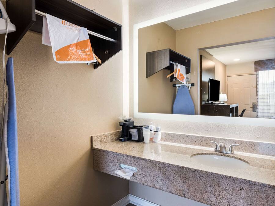 Une salle de bain d’hôtel avec un lavabo doté d’un plan de travail en granit, un miroir, un porte-serviettes et une machine à café.