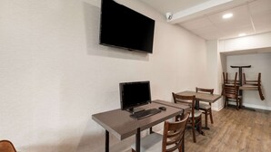 A dining area with a TV mounted on the wall, a computer on a table, and wooden chairs. - Quality Inn Gastonia East (Gastonia)