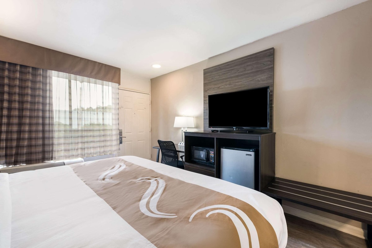 A hotel room with a bed, a television, a desk with a chair, and a microwave.