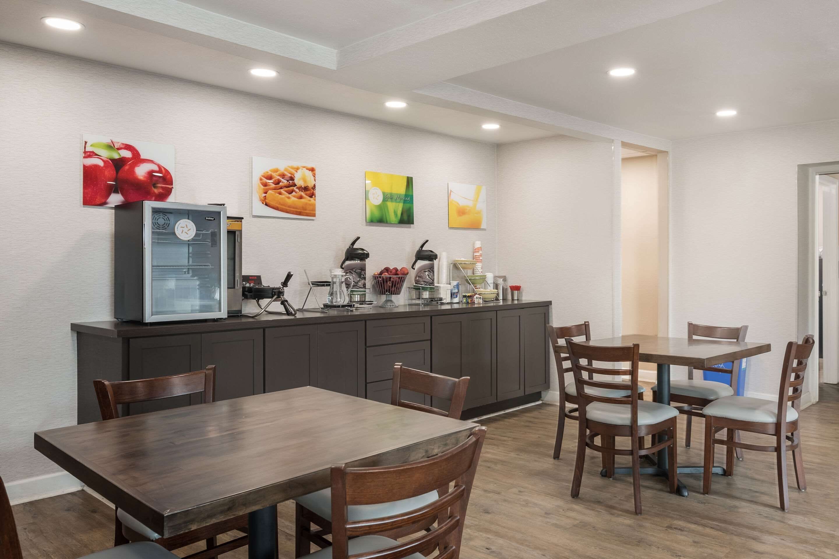 A modern kitchen with a refrigerator, microwave, and coffee maker. There are wooden chairs and a dining table.