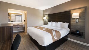 A hotel room with a bed, bedside tables, a desk, and a mirror. - Quality Inn Gastonia East (Gastonia)