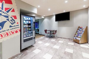 Una máquina expendedora, una pequeña mesa con dos sillas, un televisor de pantalla plana montado en la pared y un mueble para revistas.