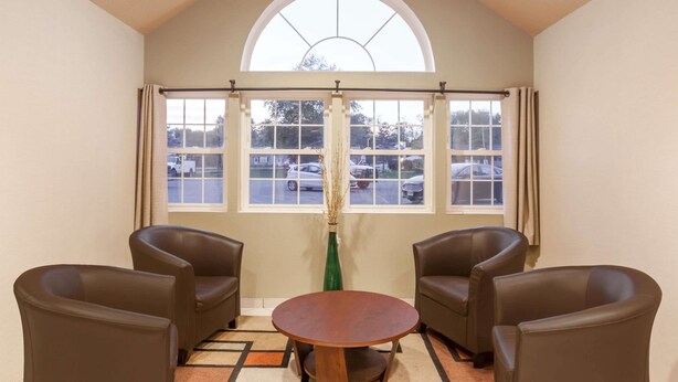 A room with a high arched window, a round wooden table, and four brown leather chairs. - Super 8 by Wyndham Schenectady/Albany Area (Schenectady)