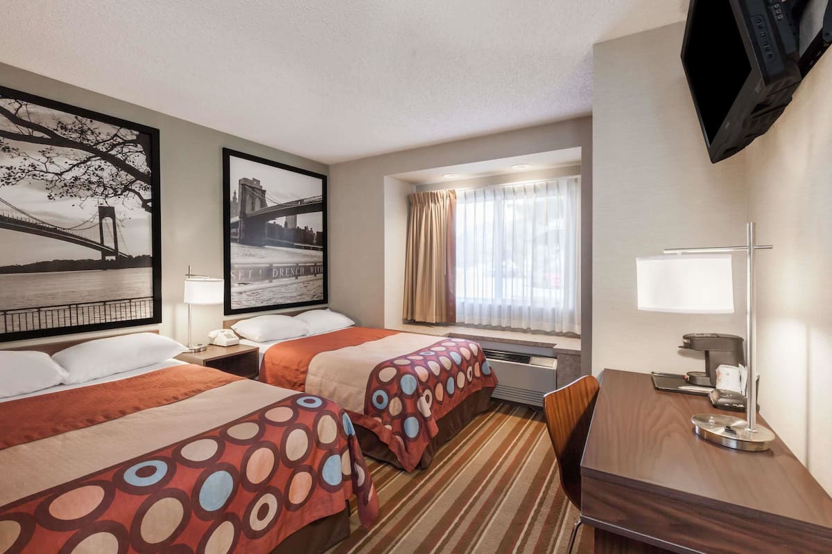 A hotel room with two beds, a desk, a TV, and a window with curtains.