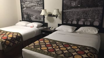 Una habitación de hotel con dos camas, cada una con una colcha de diseño diferente. Hay dos lámparas de pared y un mesita de noche con un teléfono. La habitación cuenta con grandes cuadros en blanco y negro de paisajes en las paredes.