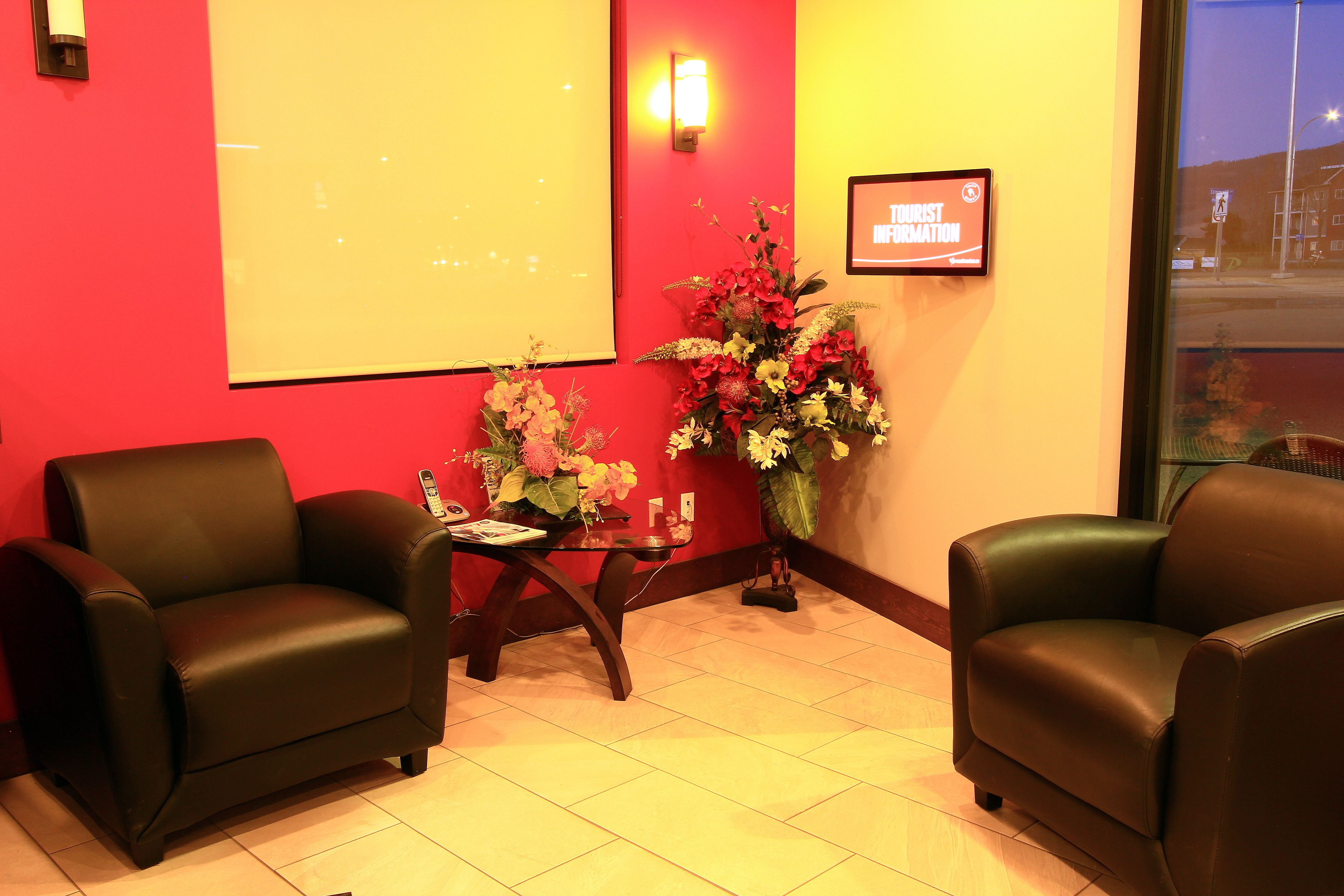 Un área de recepción con dos sofás de cuero, una mesa pequeña con un florero y una pantalla de proyector, además de un cartel que dice 'Tourist Information'.