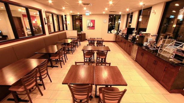 Een restaurant met meerdere houten tafels en stoelen, een balie met een koffiemachine, en een groot raam met uitzicht op de stad.