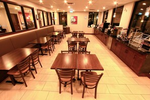 Un restaurante con varias mesas y sillas de madera, una barra con una máquina de café y un amplio ventanal con vistas a la ciudad.
